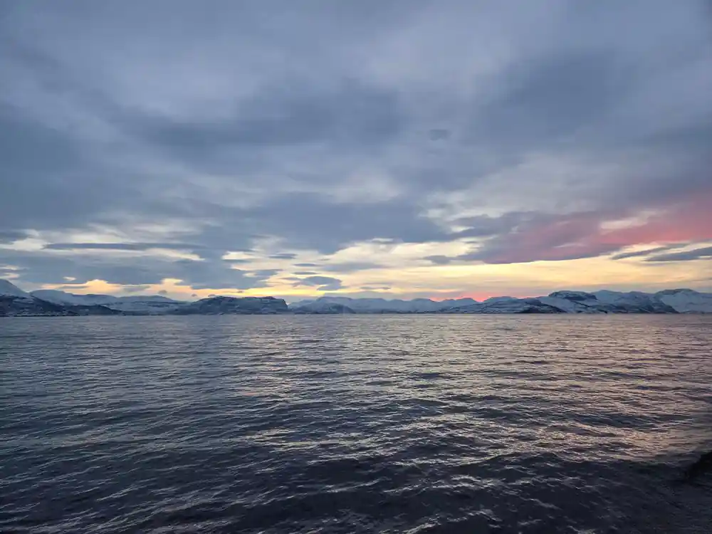 Colorful sunset sky above ocean with distant snowy peaks