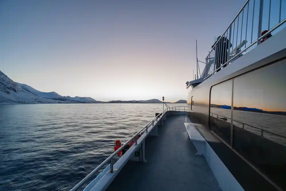 Empty boat deck and railing with mountains across calm water at dusk