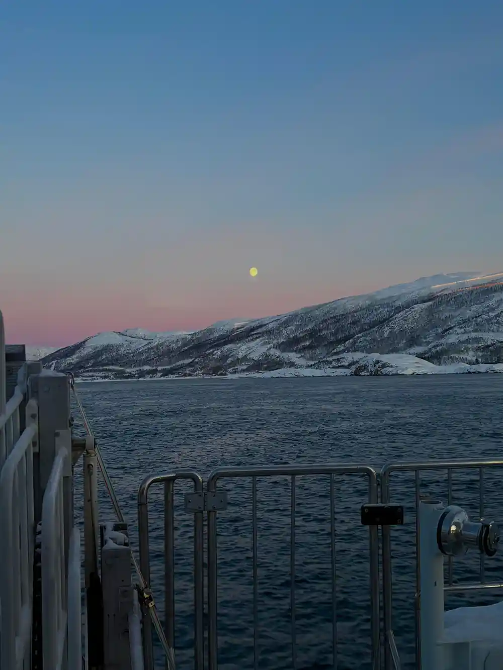 Moon rising over snowy mountains from boat at dusk
