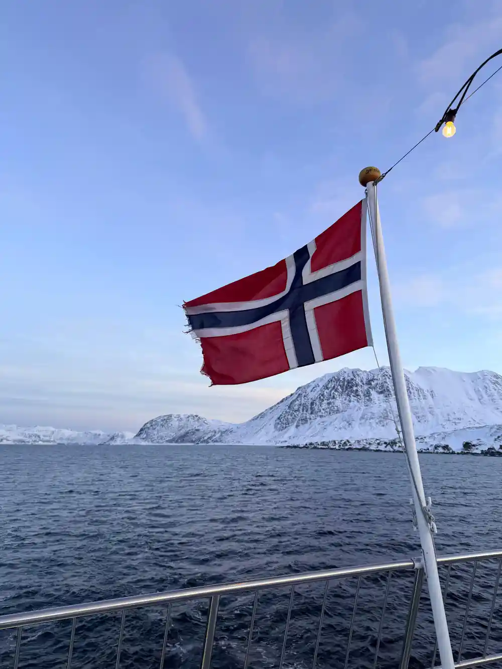 Norwegian flag on boat with snow-capped mountains in background
