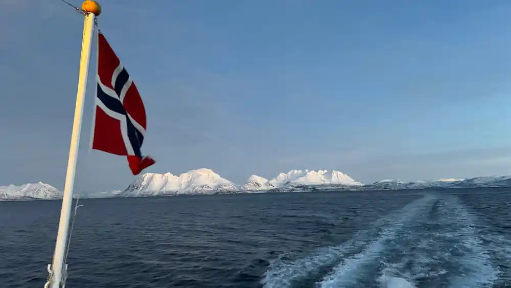 Norwegian flag on boat stern with snowy mountains beyond