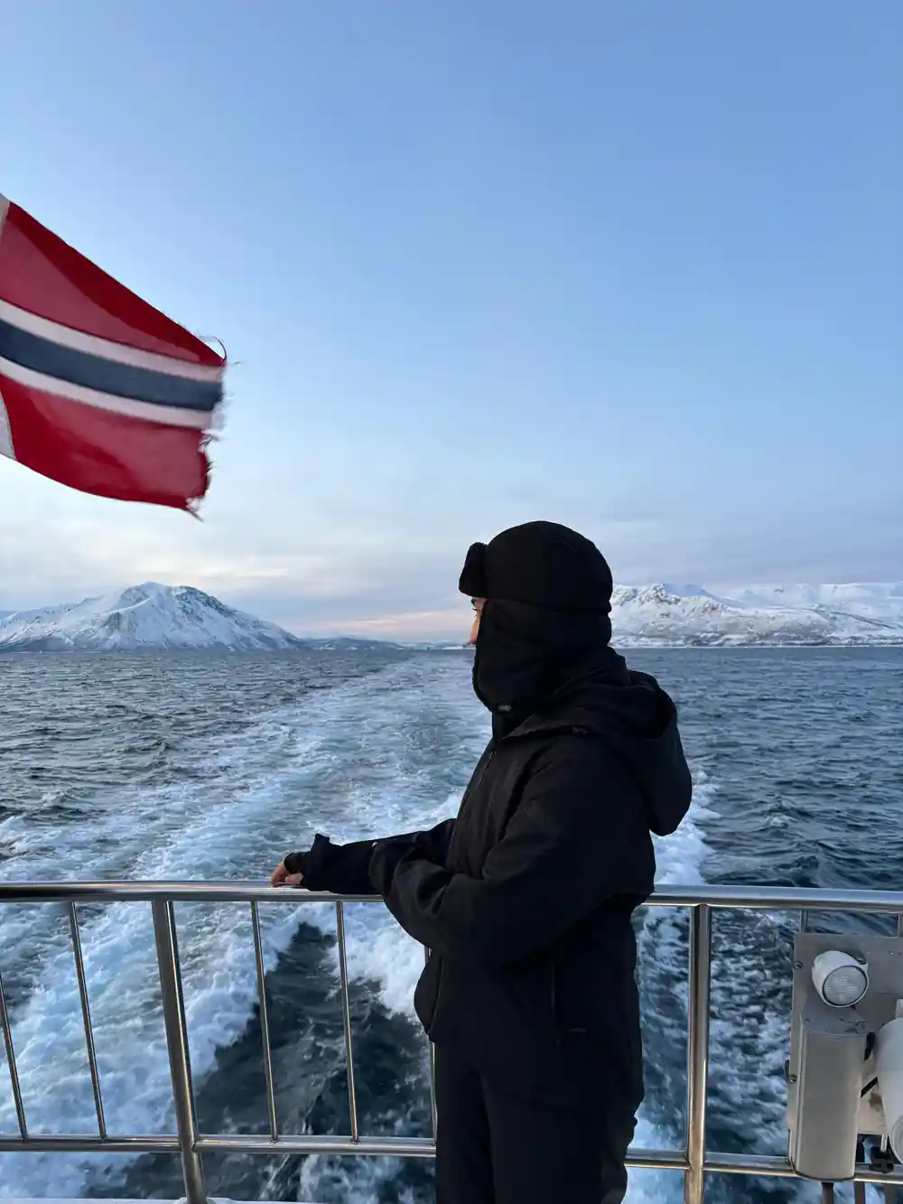 Person in black clothing at boat railing watching mountains