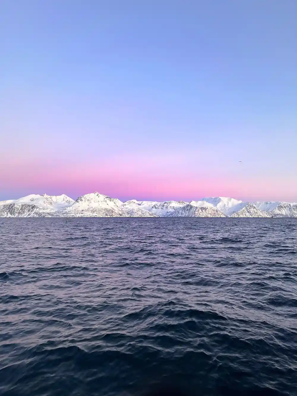Snow-capped mountains across calm sea at sunset
