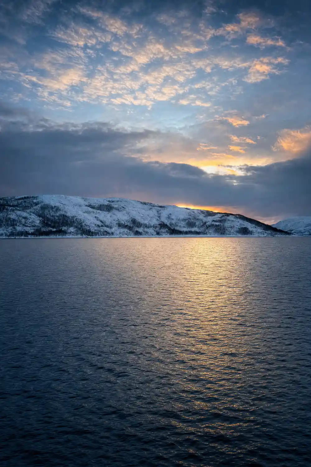 Snow-covered mountains across calm water at dusk
