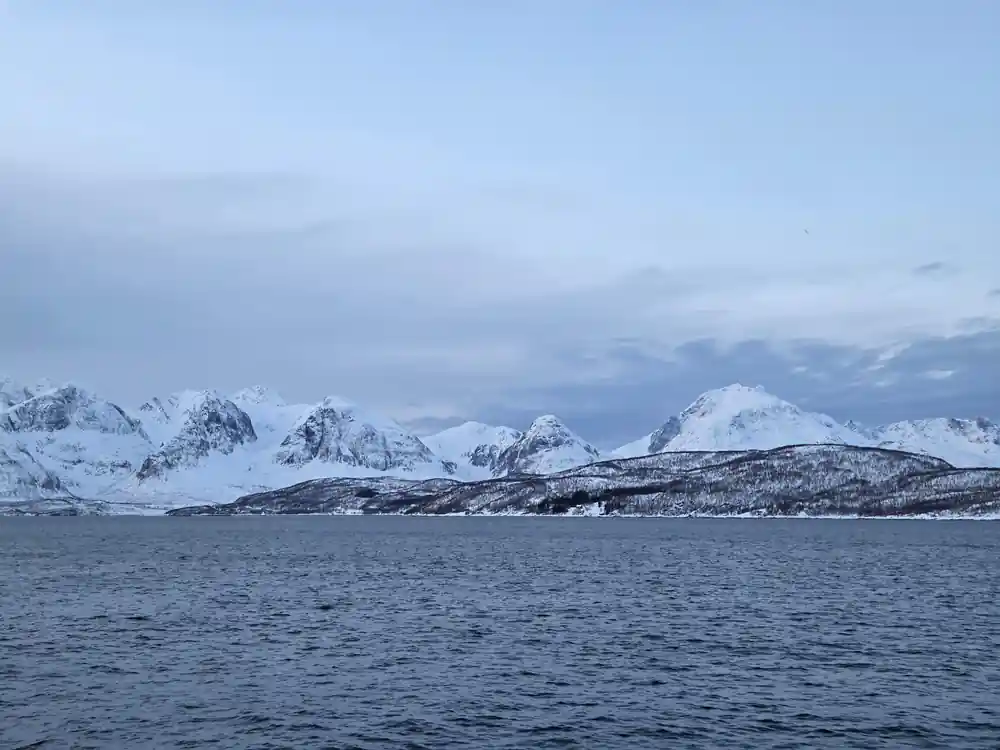 Snow-covered mountains across frozen fjord from boat railing