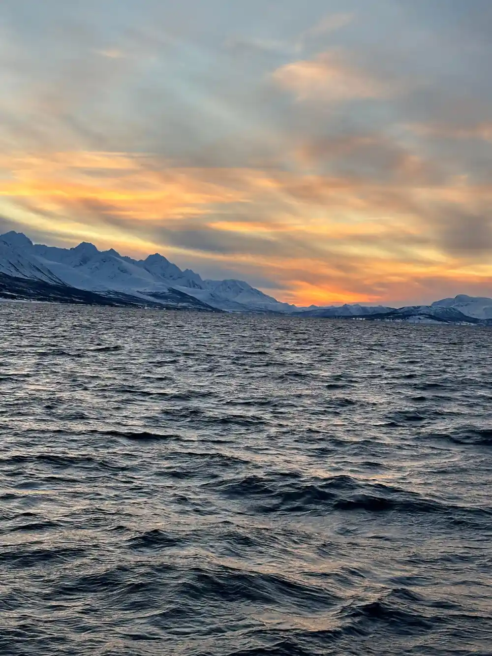 Snow-covered mountains across water at golden sunset