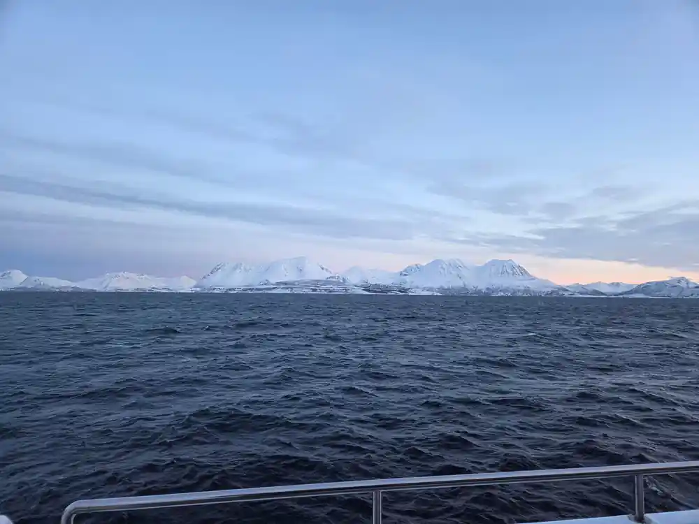 Snowy mountain range across calm water under cloudy sky