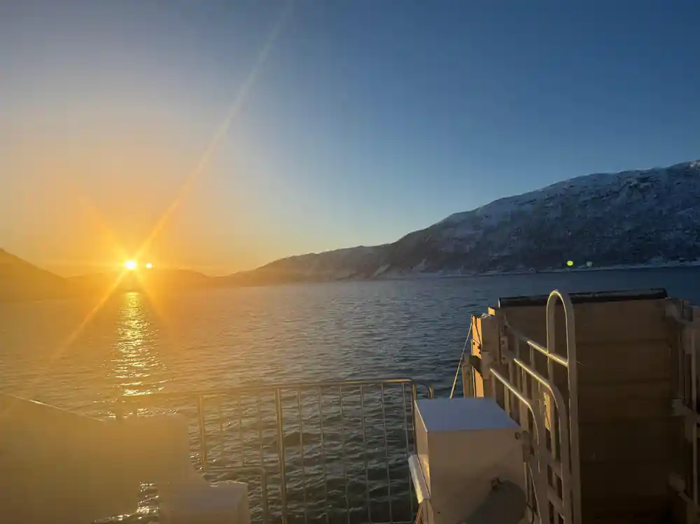 Sunrise over fjord seen from boat railing with mountains
