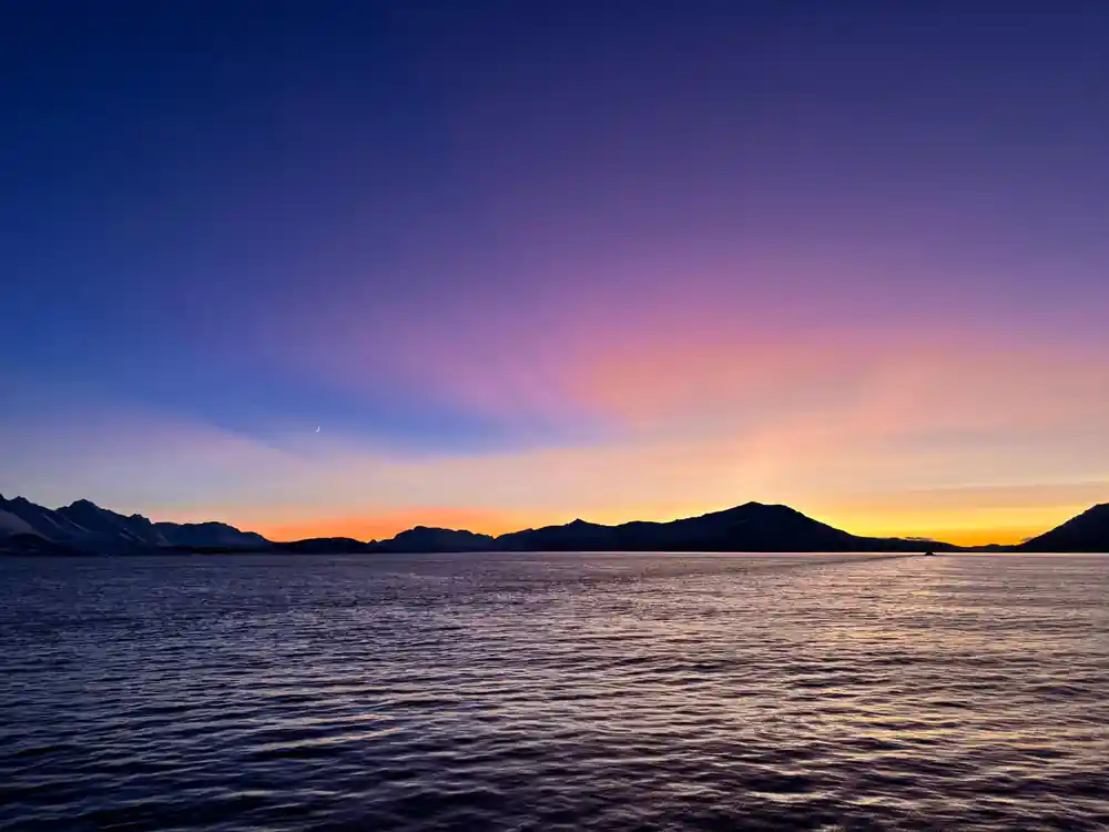 Sunset over water with mountains silhouetted against sky