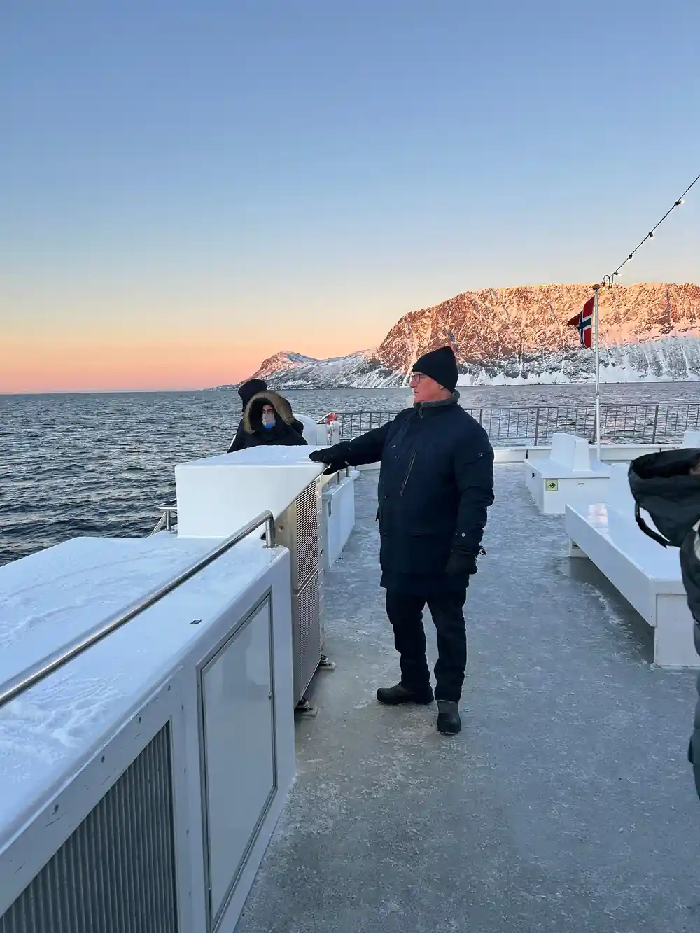 Two people standing on boat deck at dusk facing mountains