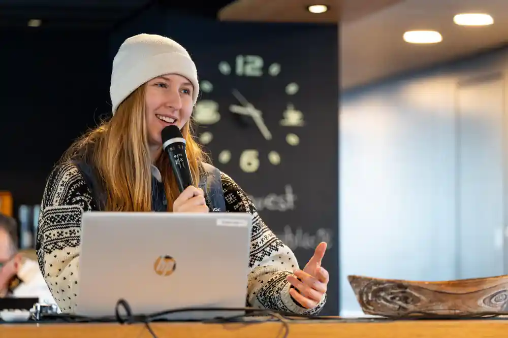 Woman in white beanie speaking at laptop presentation